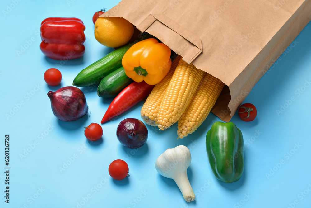 Paper bag with fresh vegetables on blue background