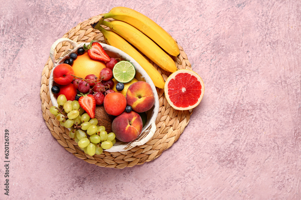 Wicker basket with different fresh fruits on pink table