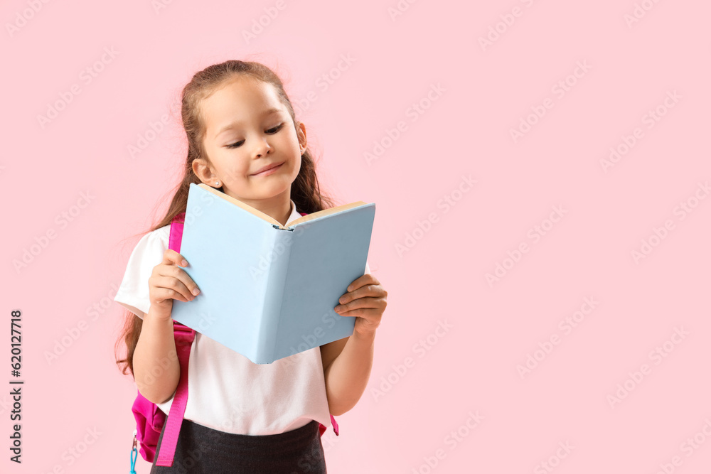 Little schoolgirl with book on pink background