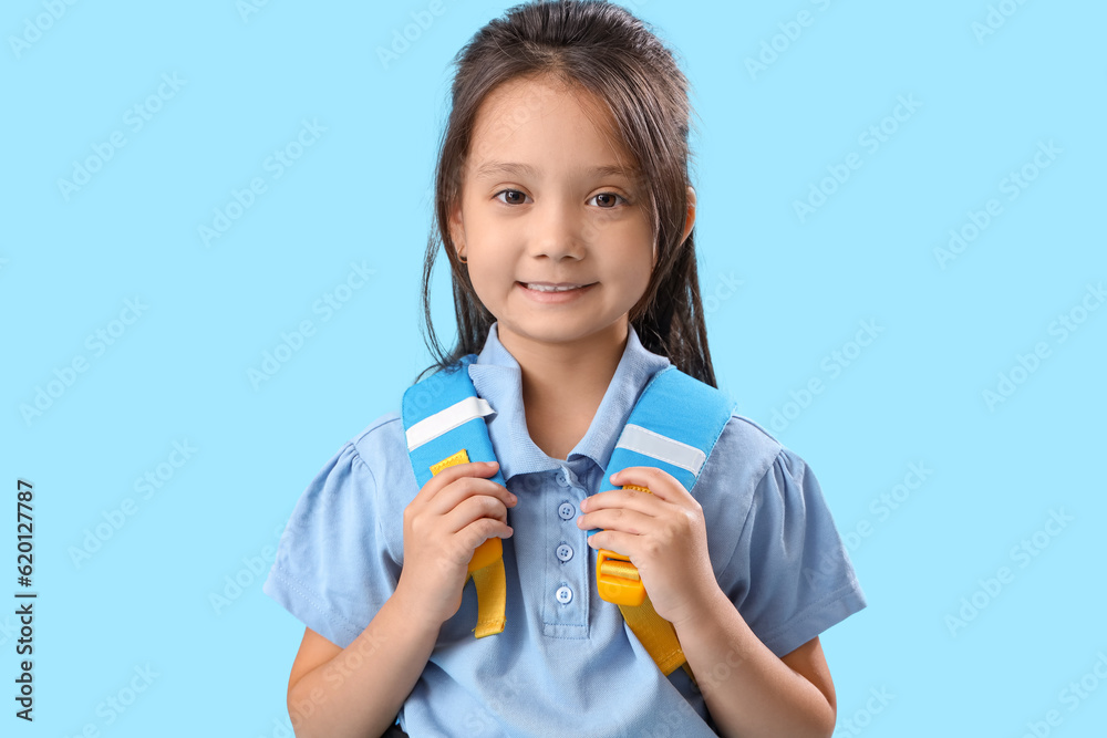 Little schoolgirl with backpack on light blue background