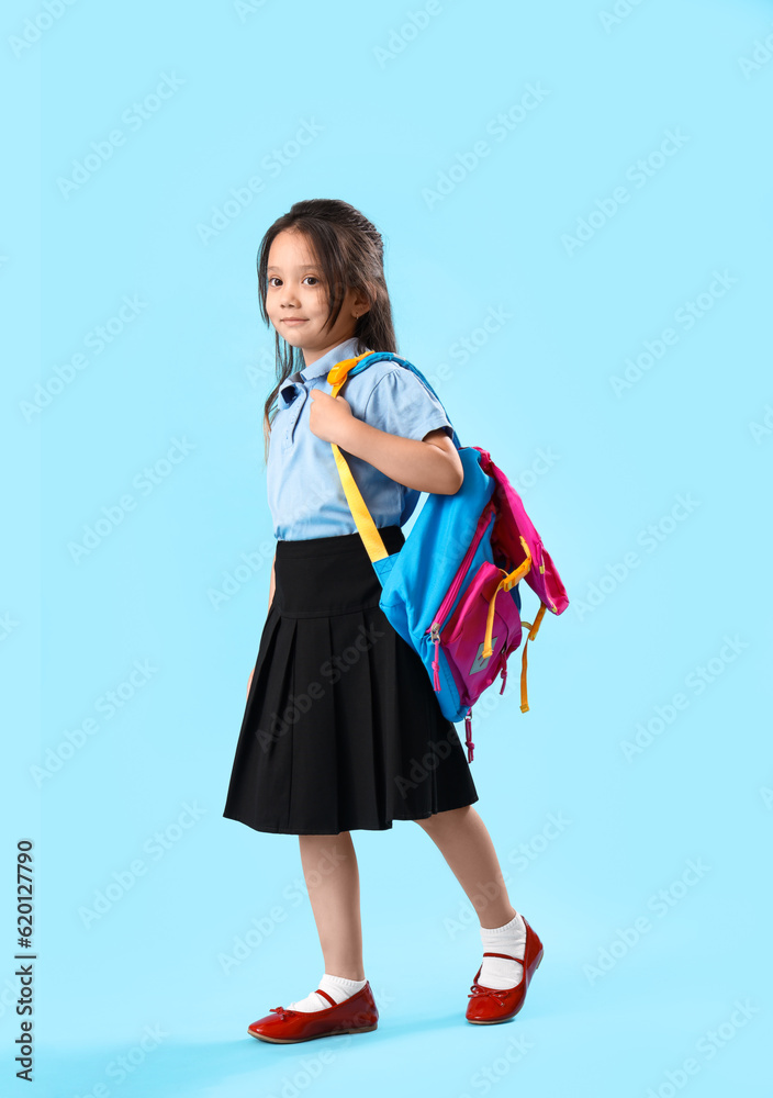 Little schoolgirl with backpack on light blue background