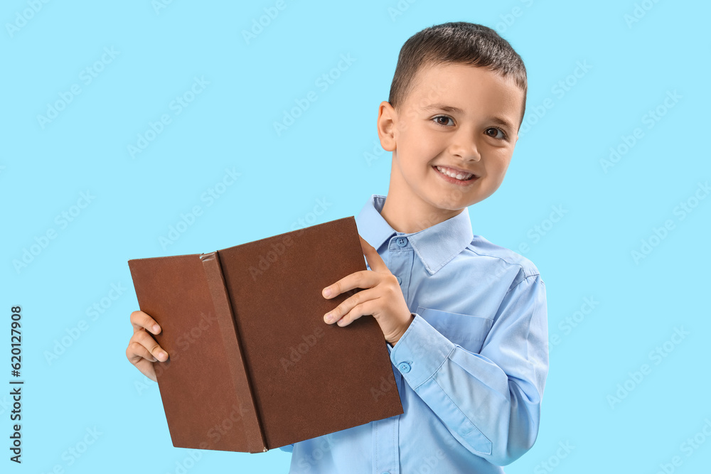 Little schoolboy with book on light blue background