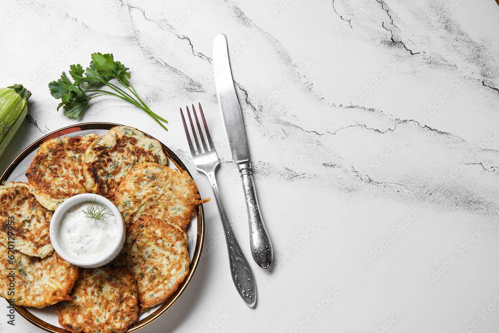 Plate of tasty zucchini fritters with sour cream on white marble background