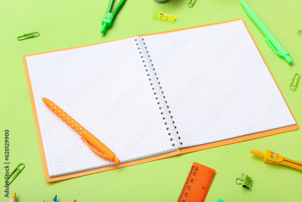 Blank notebook and different stationery on green background