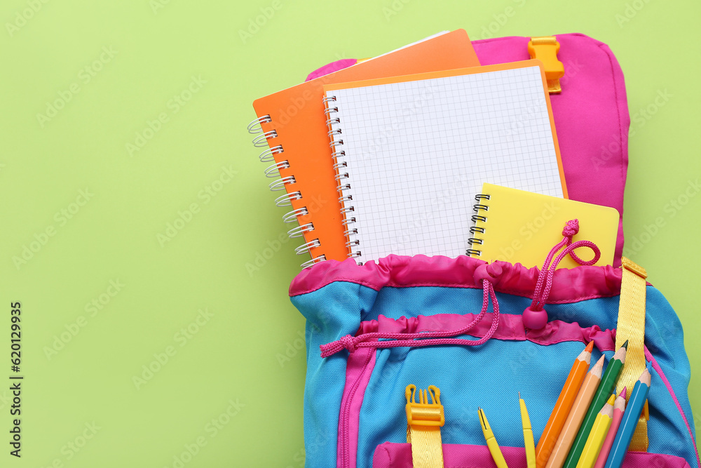 Backpack with blank notebook and stationery on green background