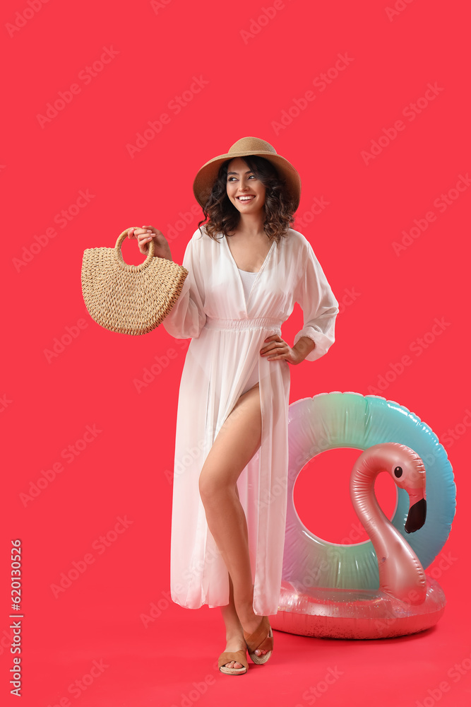 Young woman with beach bag and inflatable rings on red background