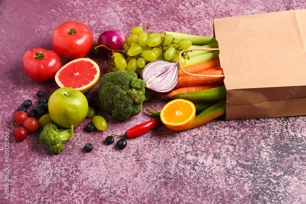 Paper bag with different fresh fruits and vegetables on purple background