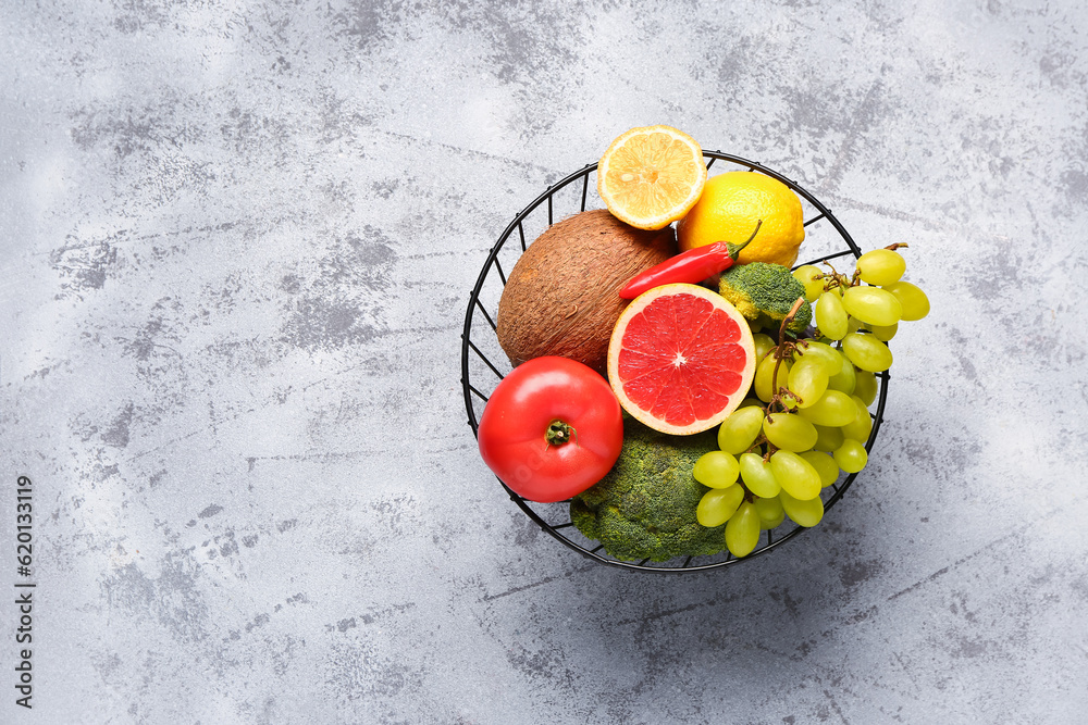 Basket with different fresh fruits and vegetables on grey background