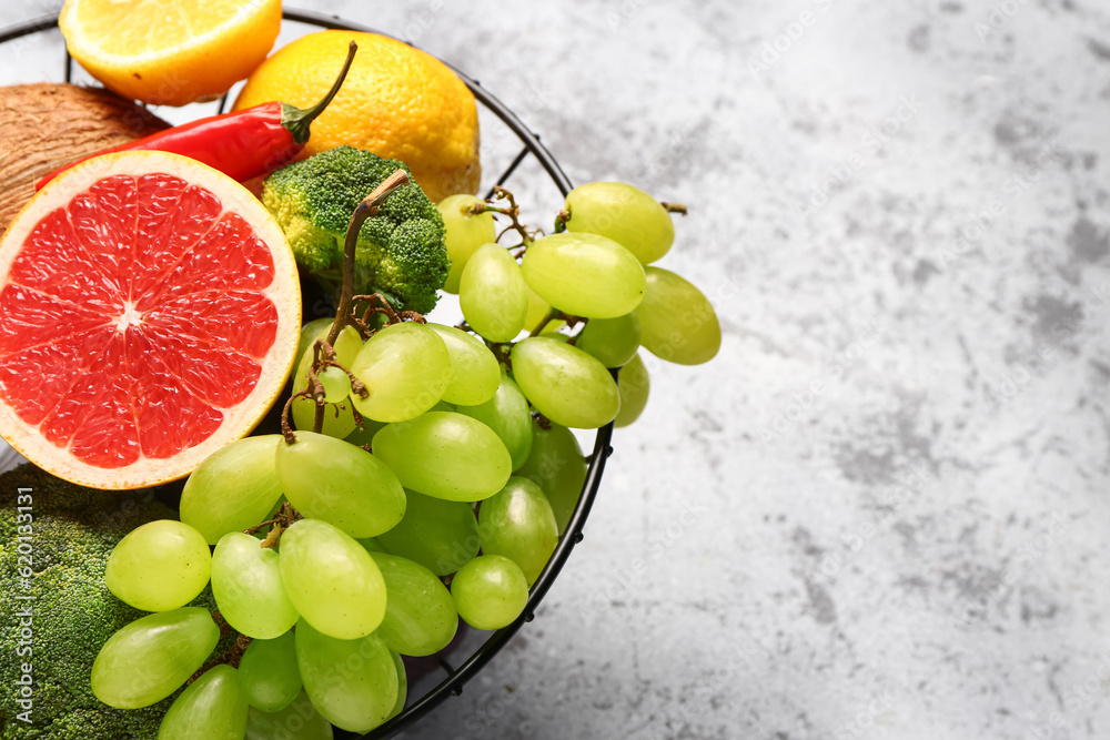 Basket with different fresh fruits and vegetables on grey background, closeup