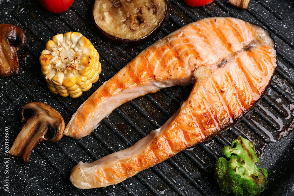 Tasty grilled salmon steak with vegetables in frying pan, closeup