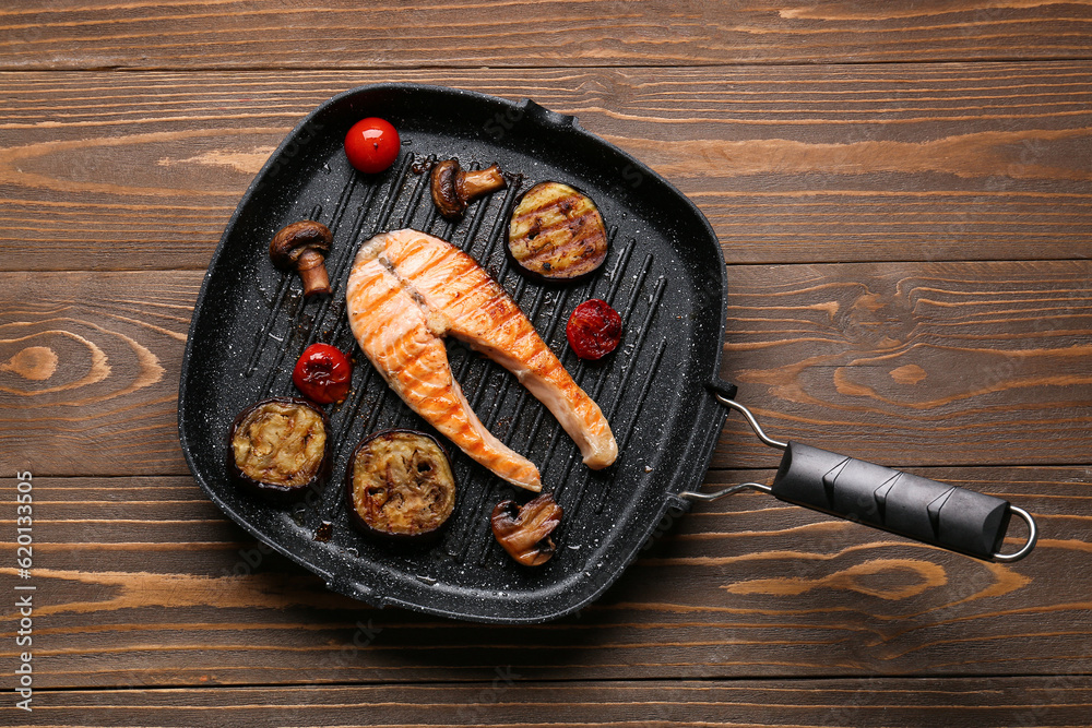 Frying pan with tasty grilled salmon steak and vegetables on wooden background