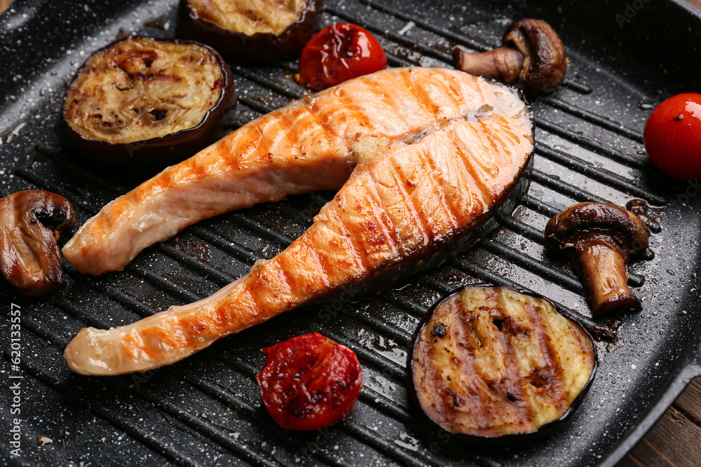 Tasty grilled salmon steak with vegetables in frying pan, closeup