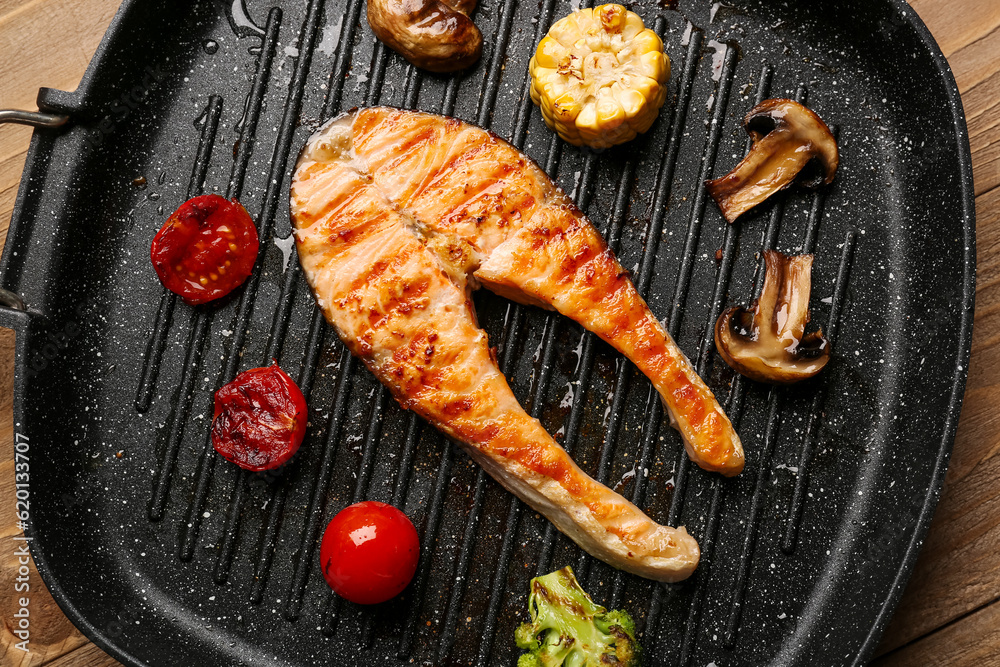 Frying pan with tasty grilled salmon steak and vegetables on table