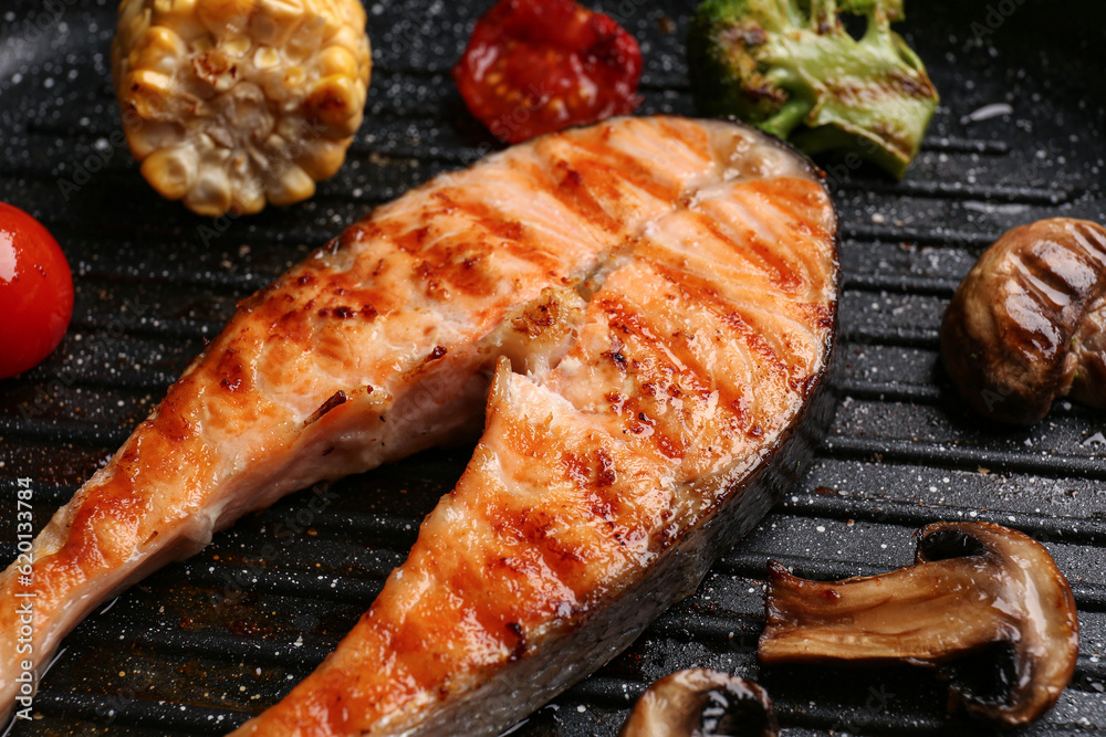 Tasty grilled salmon steak with vegetables in frying pan, closeup