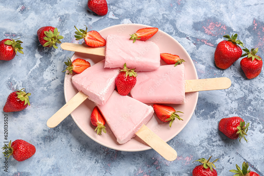 Plate with sweet strawberry ice-cream popsicles on blue background