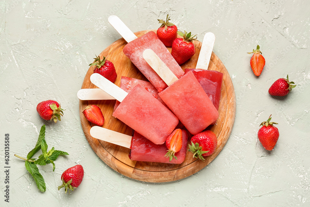 Wooden board with sweet strawberry ice-cream popsicles on grey background