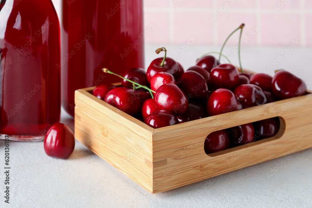 Bottles of sweet cherry liqueur and wooden box with fresh berries on white table