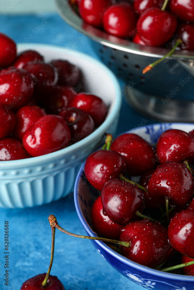 Bowls and colander with sweet cherries on blue table, closeup