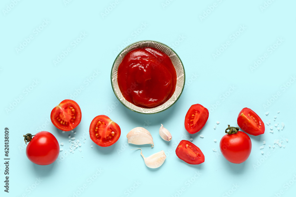 Bowl with tomato paste and fresh vegetables on blue background