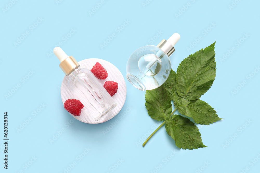 Decorative podium with bottles of cosmetic raspberry oil on blue background