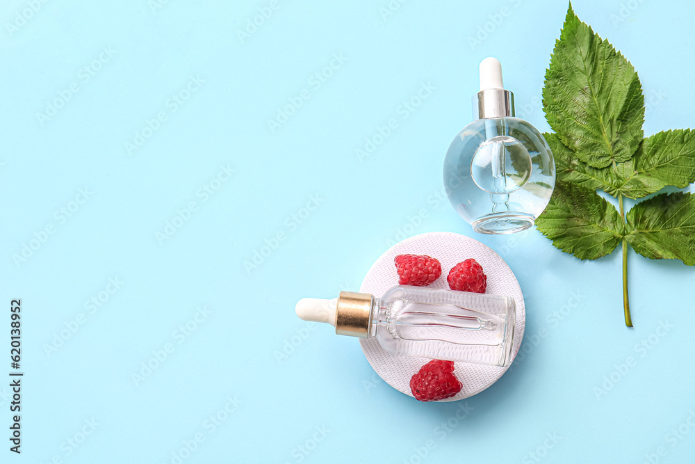 Decorative podium with bottles of cosmetic raspberry oil on blue background