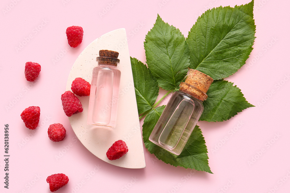 Decorative podium with bottles of cosmetic raspberry oil on pink background