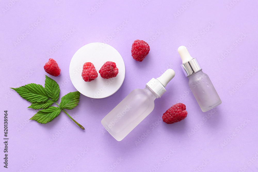 Bottles of cosmetic raspberry oil on lilac background