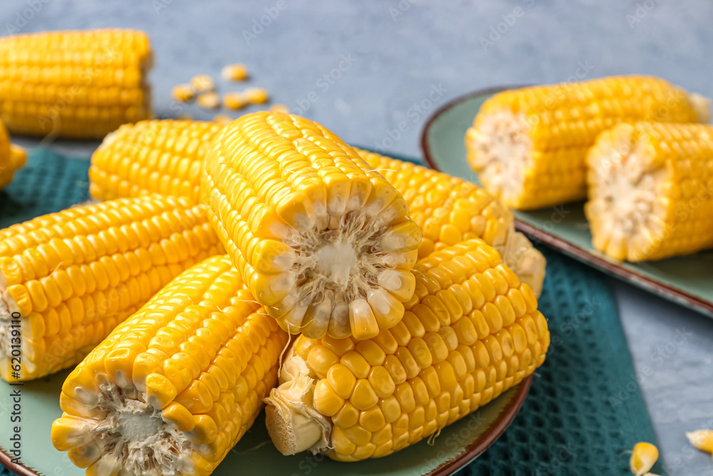 Plates with cut fresh corn cobs on blue background