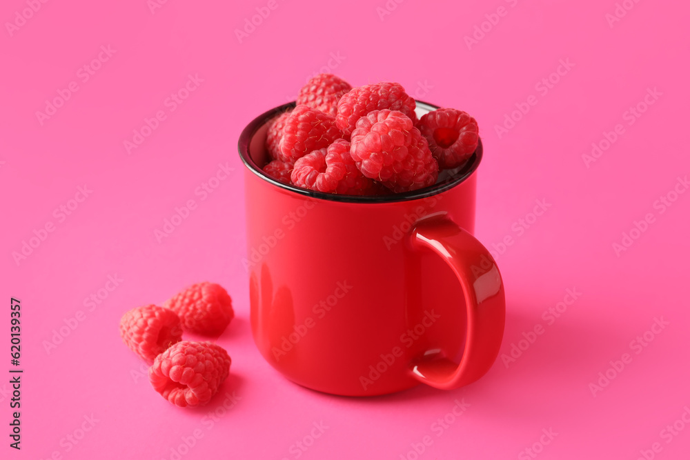 Cup with fresh raspberries on pink background