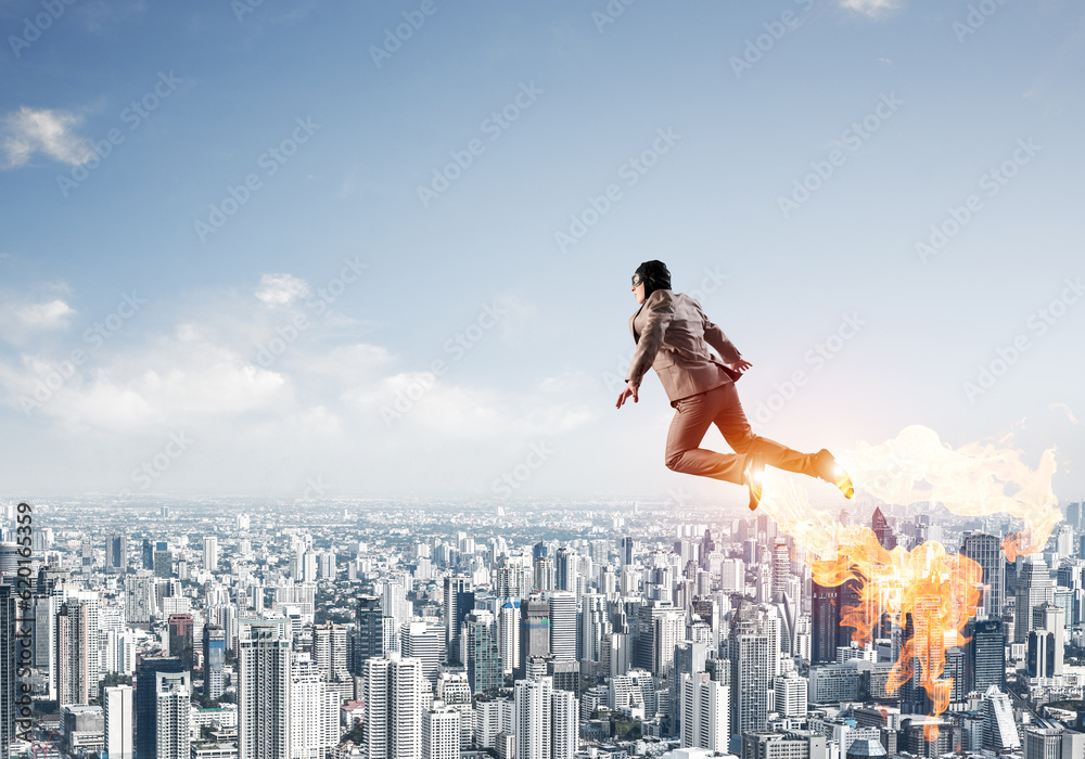 Businessman in suit and aviator hat flying in sky