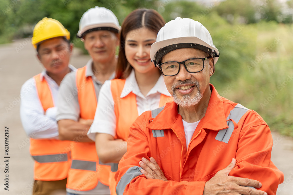 Group of happy 3 males and 1 female engineers wearing orange jumpsuit, hardhat and safety vest smili