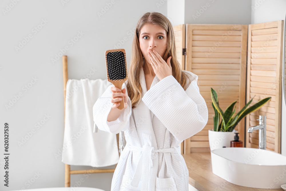 Shocked young woman with hair loss problem and brush in bathroom