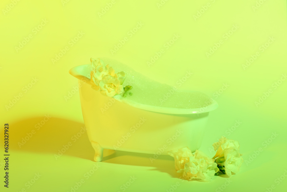 Small bathtub with foam and beautiful flowers on yellow background