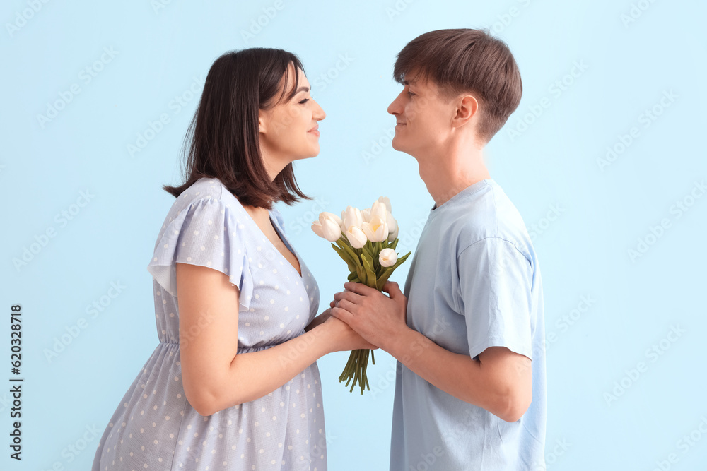 Young pregnant couple with tulips on blue background