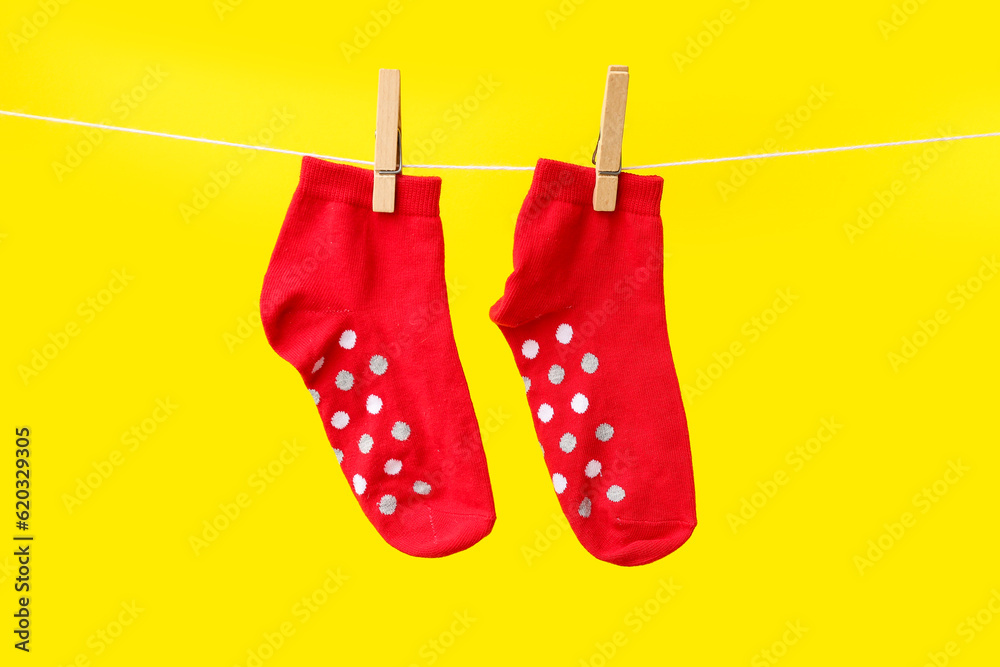 Pair of red cotton socks hanging on rope against yellow background