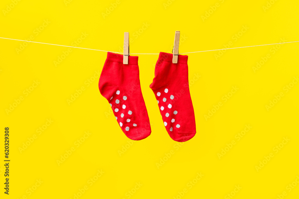 Pair of red cotton socks hanging on rope against yellow background