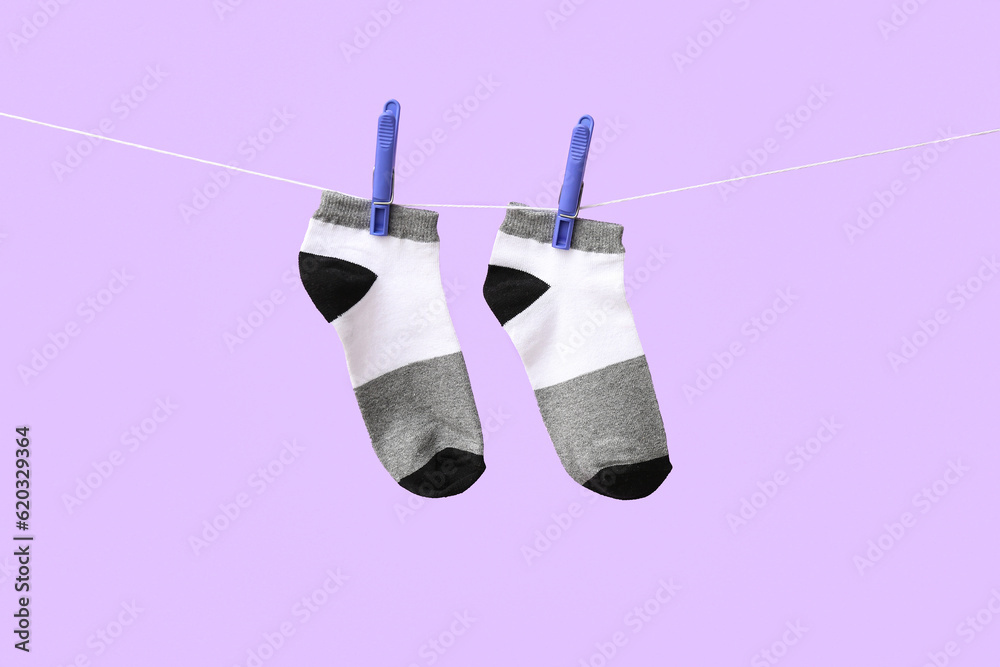 Pair of cotton socks hanging on rope against lilac background