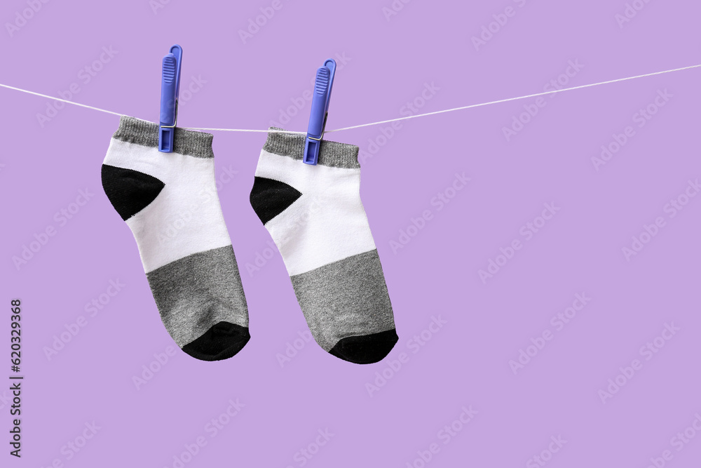 Pair of cotton socks hanging on rope against lilac background