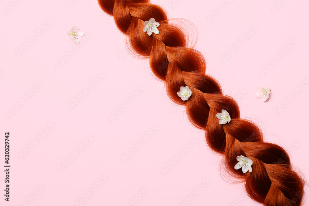 Braided ginger hair with flowers on color background, closeup