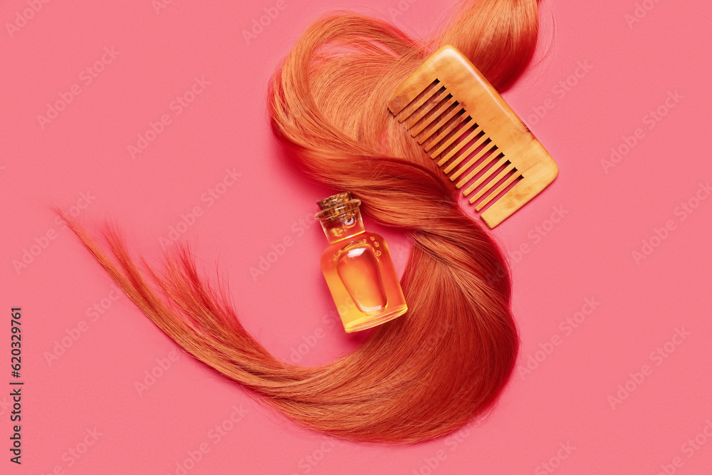 Ginger hair strand, comb and bottle of essential oil on red background