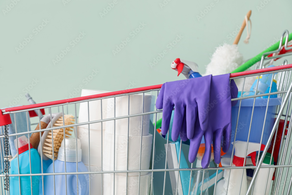 Shopping cart full of cleaning supplies on pale green background