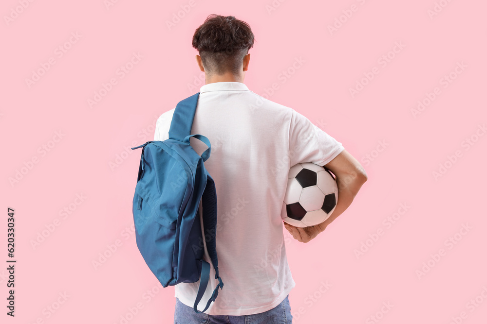 Male student with backpack and soccer ball on pink background, back view