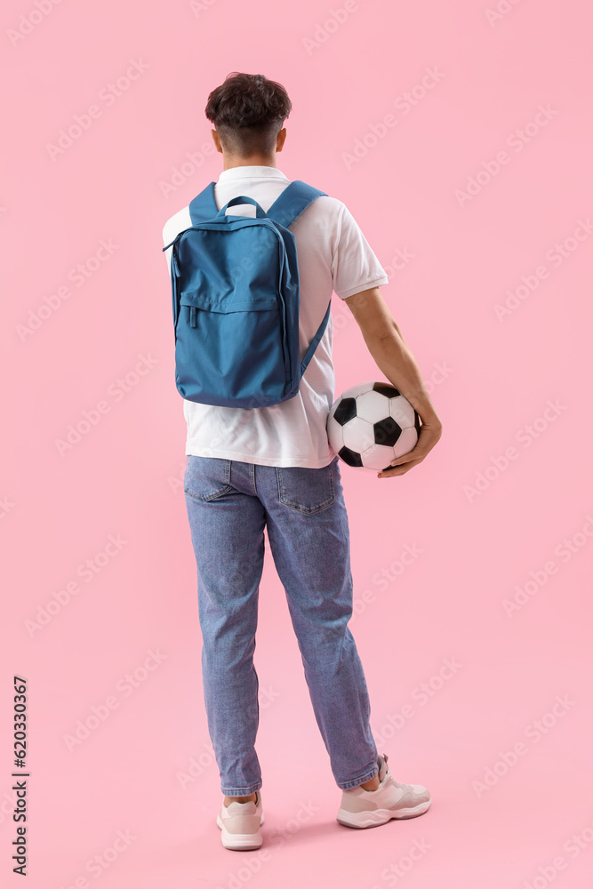 Male student with backpack and soccer ball on pink background, back view