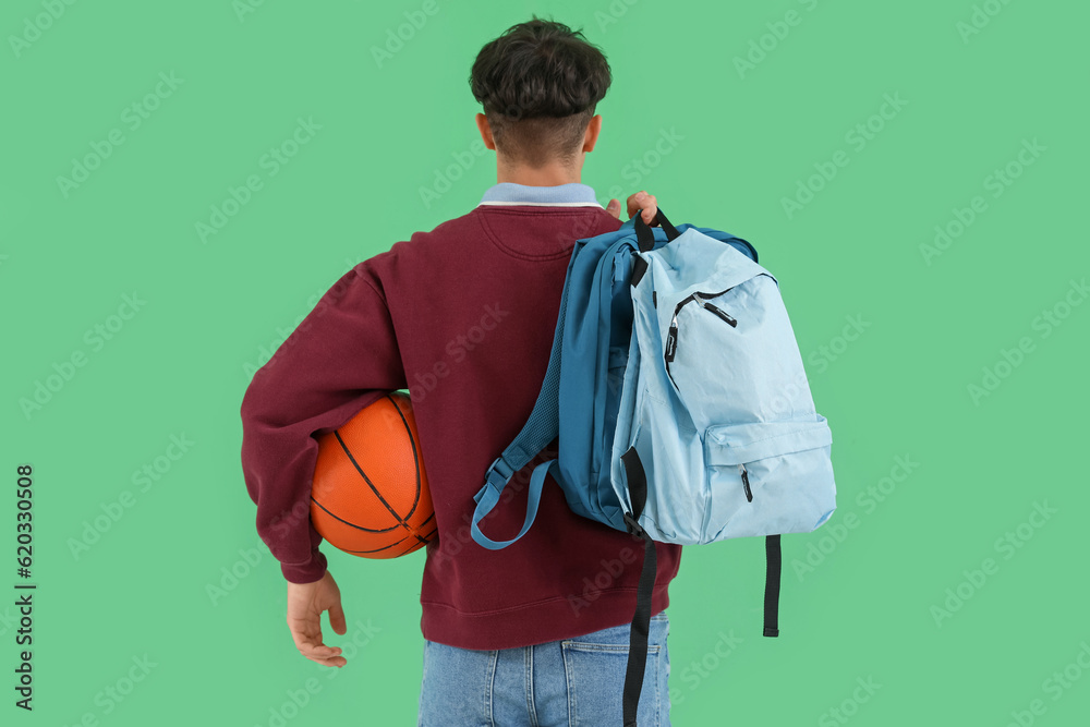 Male student with ball and backpacks on green background, back view