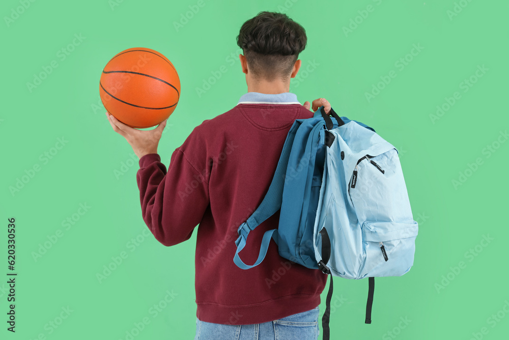 Male student with ball and backpacks on green background, back view