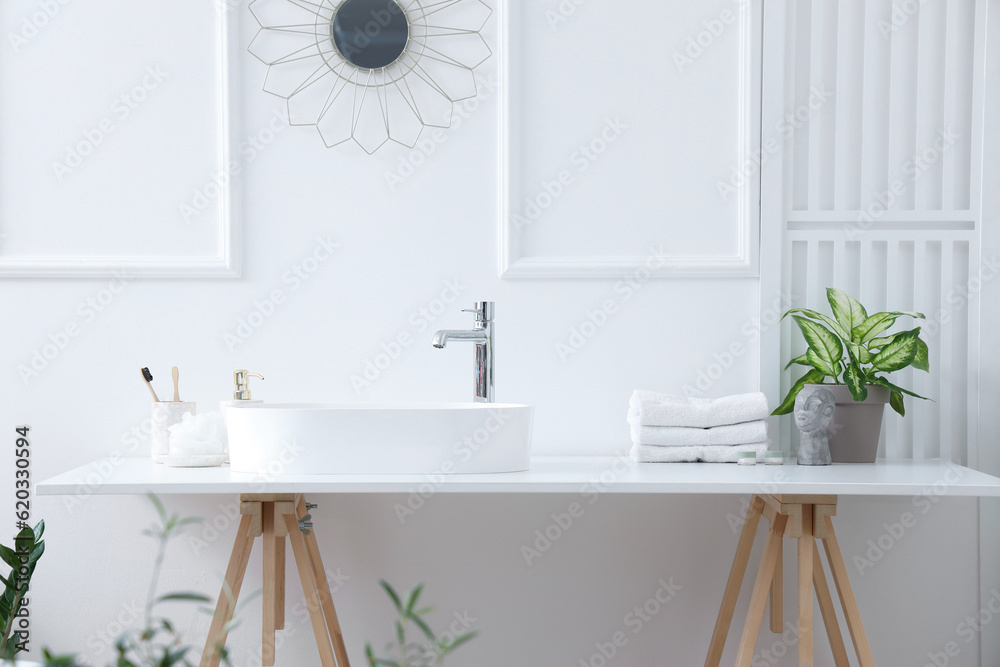 Interior of light bathroom with white sink, bath accessories and houseplants