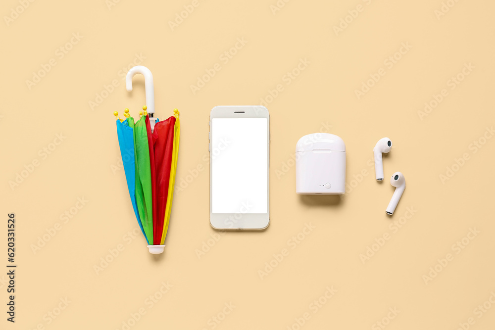 Umbrella with mobile phone and earphones on beige background. Weather forecast concept