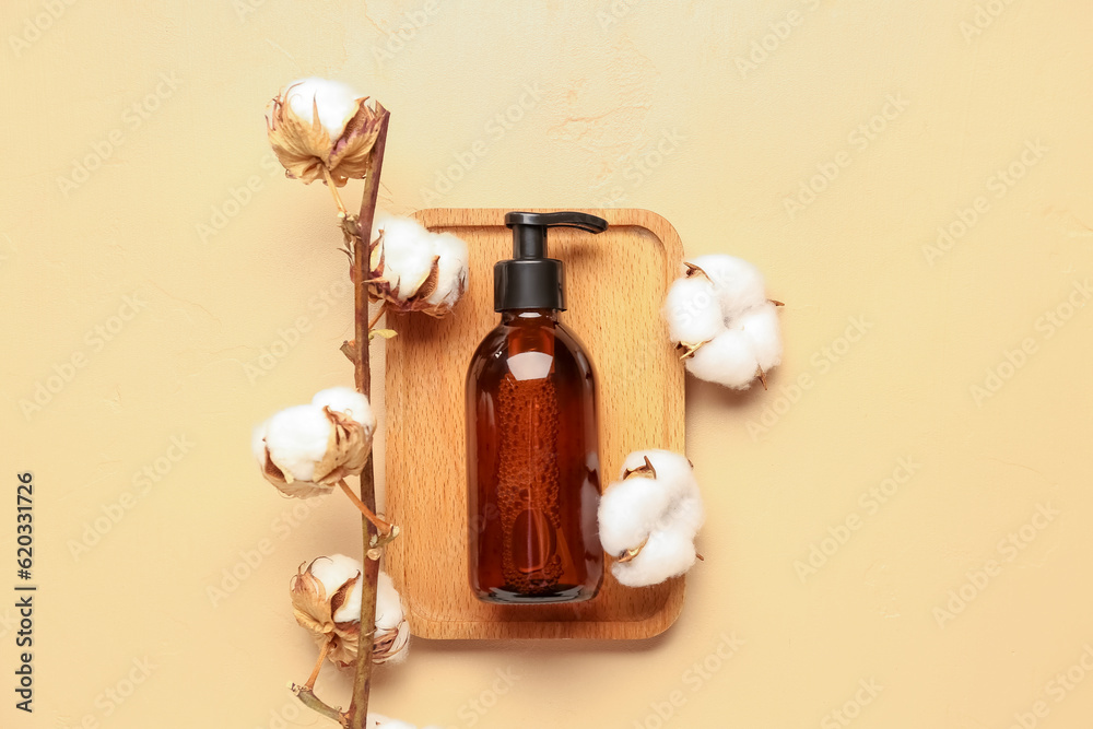 Wooden board with bottle of cosmetic product and cotton branch on color background