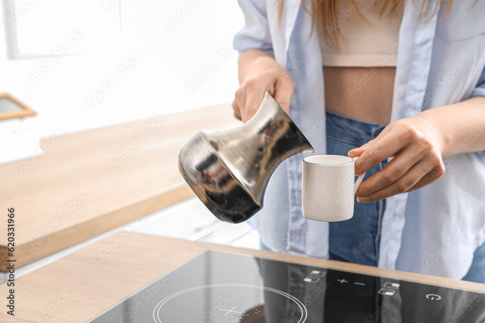 Woman pouring fresh coffee from jezve into cup in kitchen