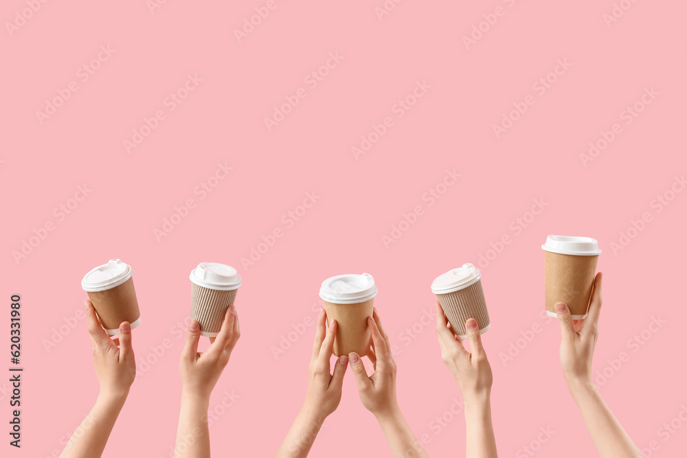 Female hands holding takeaway cups of coffee on pink background